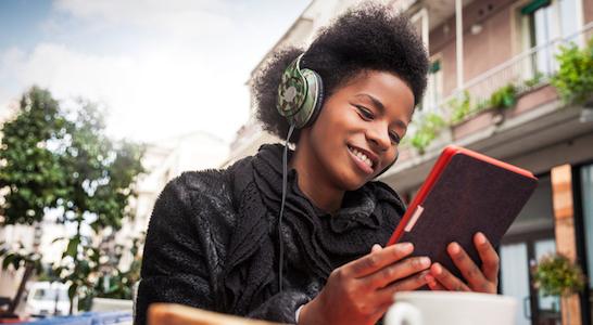 young girl listening to books with headphones on a tablet