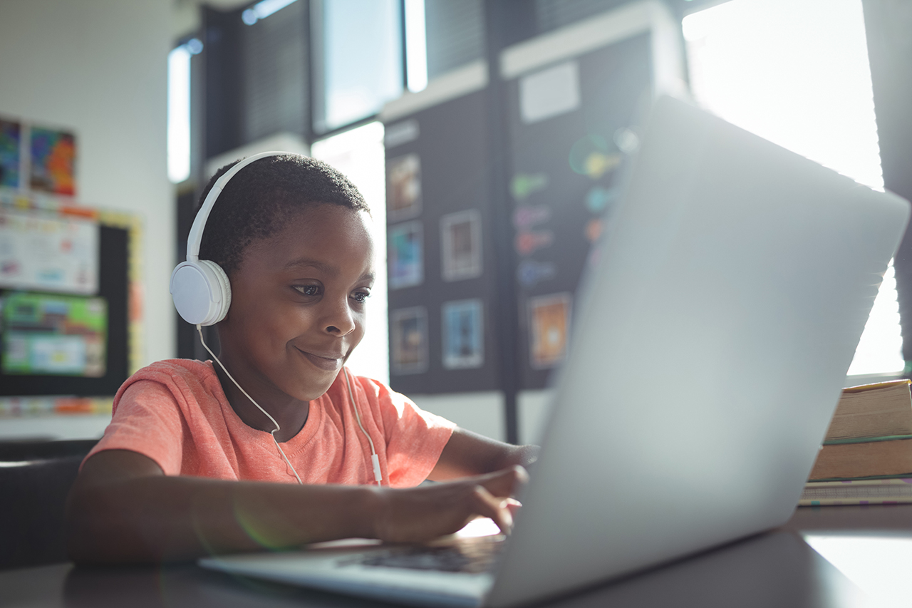 Elementary boy using headphones and laptop in classroom