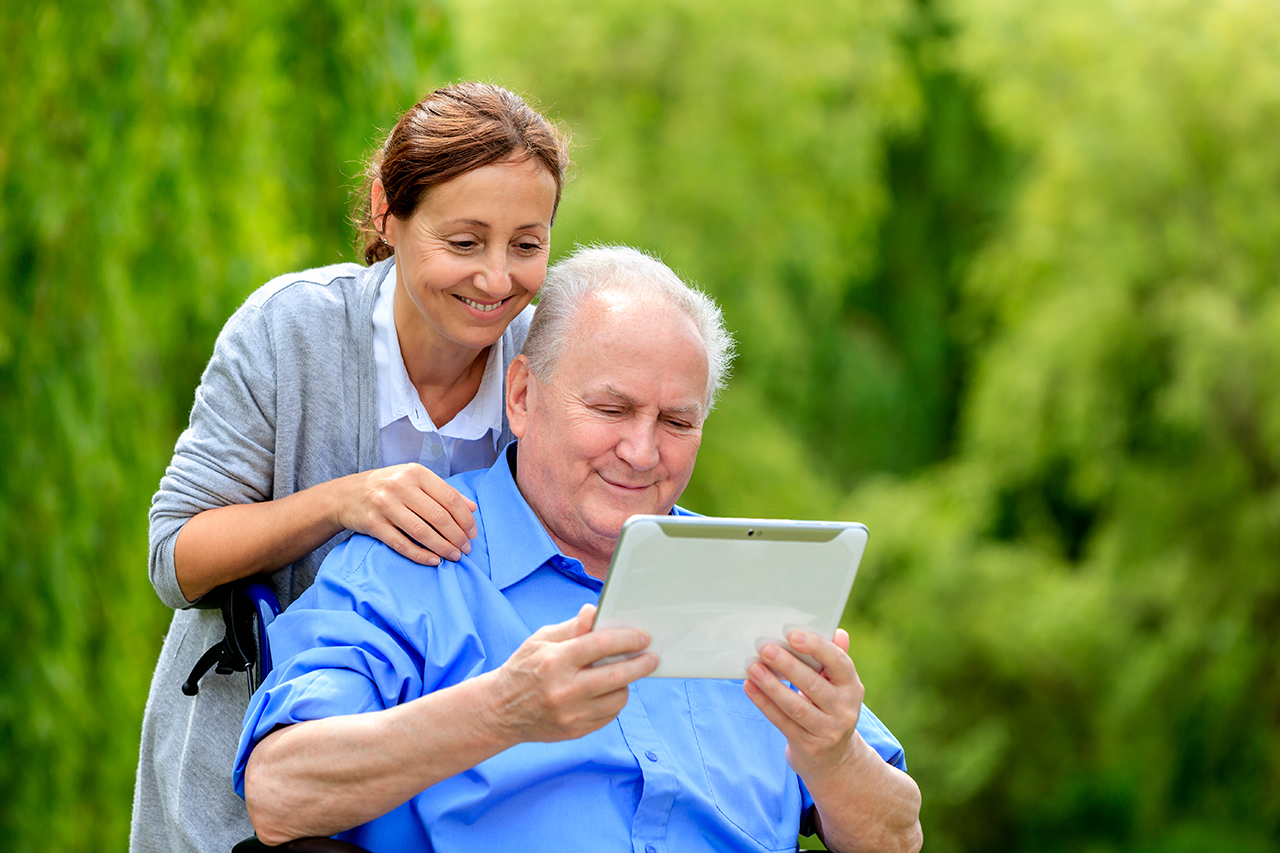 Caregiver lays her hand on shoulder of senior holding a tablet on a wheelchair