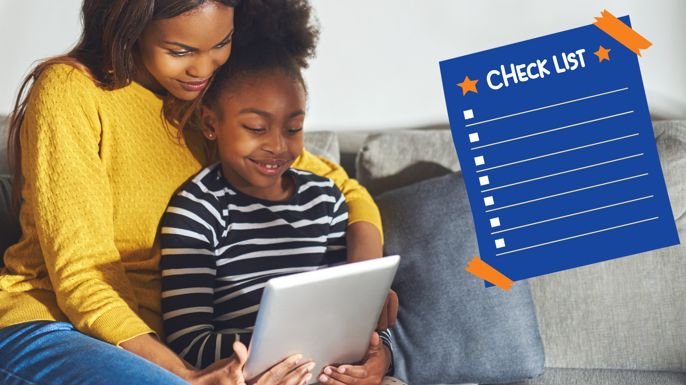 Parent and child smiling while reading on a tablet and seated on a sofa.