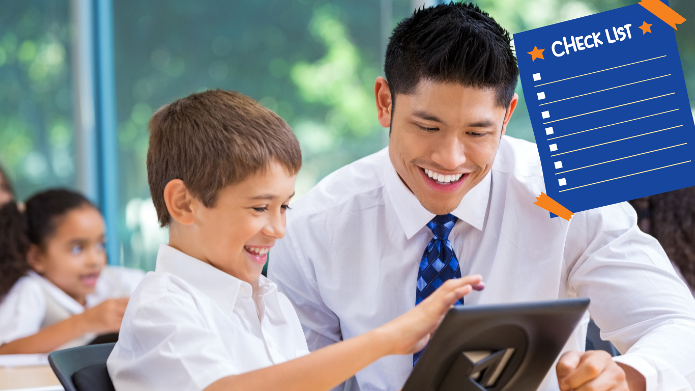 teacher helping student who is reading on tablet in a classroom.