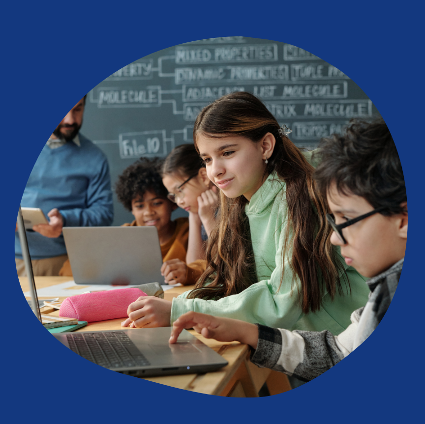 image: students in a classroom on laptops learning with a teacher in the background.