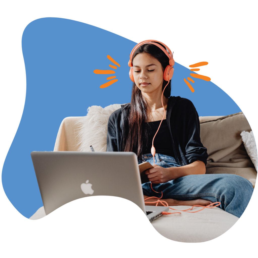 Teen female student reading on laptop with headphones sitting on couch.